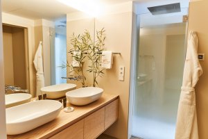 helles badezimmer in beigen tönen und zwei waschbecken vor der großen dusche im 7 pines hotel auf ibiza