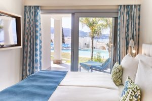 großes bett einer laguna suite im 7 pines hotel auf ibiza mit blick in den garten durch die großen bodentiefen fenster