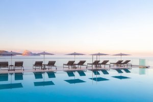 großer und moderner infinity pool bei sonnenuntergang mit blick auf das mittelmeer und bequemen sonnenliegen im 7 pines hotel auf ibiza