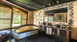 helles badezimmer mit großer badewanne mit holzverzierungen in einer garden villa des Alfajiri Villas hotel an diani beach in kenia