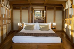 großes doppelbett mit offenem badezimmer am kopfende in der luxuskabine auf dem schiff amandira von aman resorts