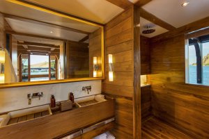 luxuriöses bad in der doppelkabine auf dem luxusschiff amandira von aman resorts mit doppelwaschbecken und edler holzverkleidung mit blick auf das meer durch das fenster in der dusche