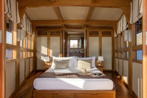 großes doppelbett einer kabine auf dem luxusschiff amandira mit hellen holzwänden und großen fenstern auf das offene meer
