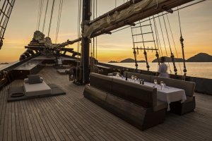 wunderschön gepflegtes Deck des luxus segelschiffes amandira von aman resorts bei untergenehnder sonne mit gedeckter langer tafel an deck mit blich auf das meer vor indonesien