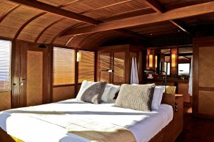 großes doppelbett der master kabine ensuite mit angrenzendem badezimmer hinter dem bett und blick auf den ozean vor indonesien für einen romantischen urlaub