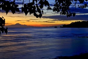 romantischer sonnenuntergang mit blick auf das meer und die küste von indonesien unter dunkelblauem himmel mit orange gelber sonne die am horizont verschwindet