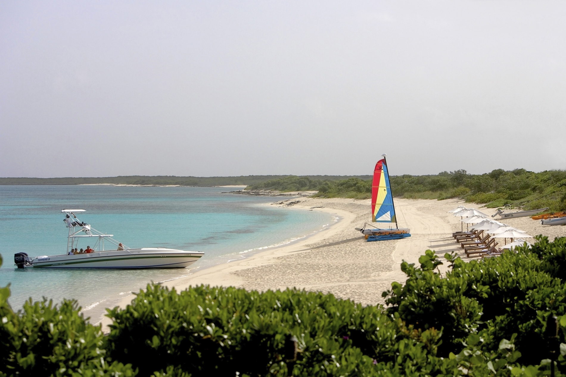 sandstrand mit boot yacht und segelboot vom luxuriösen modernen designer hotel und resort auf den turks- und caicosinseln in der karibik daneben sonnenliegen