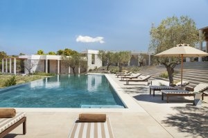 Terrasse und Pool einer 6 Zimmer Villa mit vielen Liegen, hellem Steinboden und dunkelblauem Wasser Luxusresort Griechenland