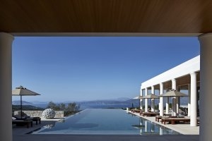 Der dunkelblaue Pool und das strahlend weiße Gebäude der Villas im Amanzoe an dem Designliegen und Schirme bereit stehen.