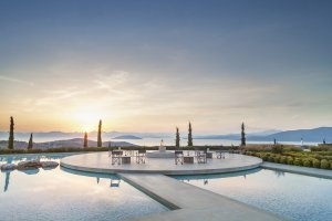 runde Terrasse die von einem Pool umgeben ist mit hellen Möbeln im Sonnenuntergang des Amanzoe in Griechenland