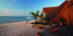 idyllischer und exotischer strand mit blauem himmel beim sonnenuntergang und palmen und bungalows mit terasse vom azura benguerra island in mosambik afrika