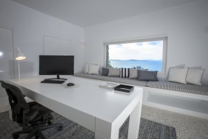 großzügiger arbeitsbereich mit schreibtisch und sitzecke for dem fenster das den blick auf das mittelmeer freigibt in der privaten big blue beach villa auf mykonos