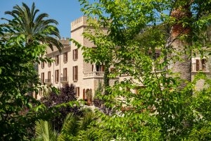 blick durch palmen und den garten auf das burghotel castell son claret auf mallorca