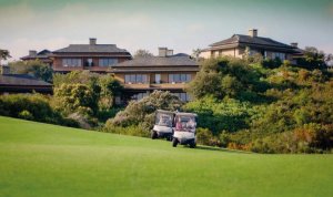 zwei golf cards auf dem golfplatz vor dem wunderschönes Golfhotel Südafrika Conrad Pezula inmitten saftig grüner natur gelegen.
