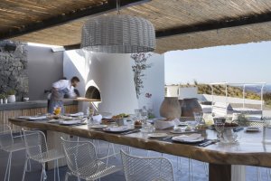 großer gedeckter esstisch auf der terrasse der privaten villa erosantorini mit außenküche und eigenem koch der in der villa für kulinarische erlebnisse sorgt