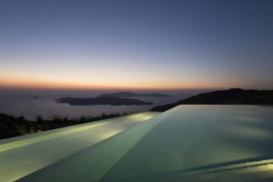 großer infinity pool in der privaten luxusvilla erosantorini bei sonnenuntergang beleuchtet auf santorin