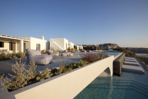 blick auf die große terrasse der privaten villa erosantorini mit großem pool direkt am meer auf santorin unter blauem himmel