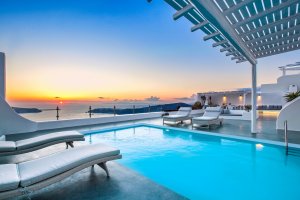 einmalig schöner sonnenuntergang auf der terrasse der luxus villa erossea mit eigenem pool und gemütlichen sonnenliegen unter dem bunt gefärbten himmel von santorini