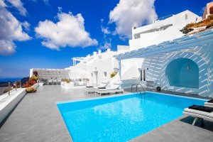 pool der modernen luxusvilla erossea auf santorini mit sonnenliegen auf der großen terrasse und hellen möbeln unter strahlend blauem himmel laden zum entspannen ein