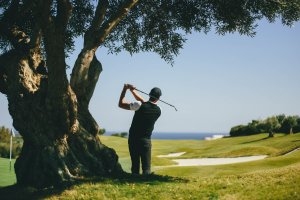 Golfspieler beim Abschlag auf dem Golfplatz der Finca Cortesin mit Blick aufs Meer und alten Bäumen auf dem Platz an der Costa del Sol