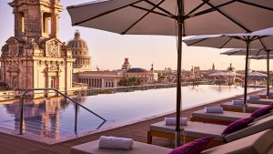 sonnenuntergang auf dem dach des luxushotels mit blick auf den großen pool umringt von sonnenliegen und der historischen stadt im hintergrund unter blauem himmel