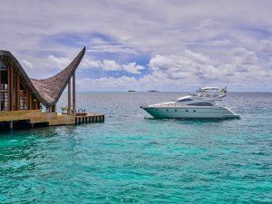 kleine yacht am anleger des luxusresorts vor dem kleinen gebäude mit geschwungenem dach im indischen ozean