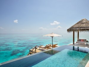 blick über den infinity pool einer villa die direkt auf dem wasser errichtet ist mit blick auf den ozean bei herrlichem sonnenschein und türkisblauem wasser