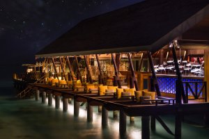 bar auf stelzen im wasser erbaut nachts beleuchtet im lux hotel auf den malediven