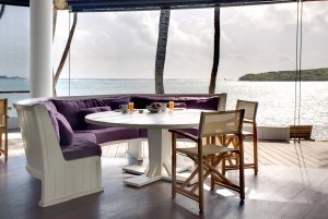 Detailaufnahme einer Sitzecke im Restaurant und das Karibische Meer im Hintergrund durch die großen Fensterflächen zu sehen im Luxushotel Karibik Le Sereno am Strand Grand Cul des Sac