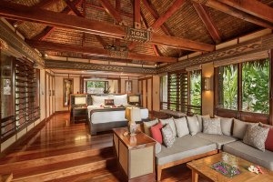 Schlafzimmer und Wohnzimmer eines Deluxe Beachfront Bure mit viel Holz und großen Fenstern im Luxushotel Likuliku Lagoon Resort auf Fiji