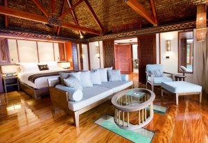 Schlafzimmer eines Over Water Zimmers mit viel Holz großem Bett und Wohnbereich im Luxushotel Likuliku Lagoon Resort