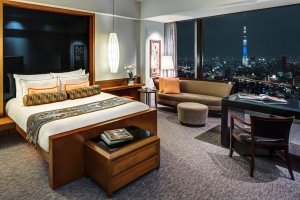 Bett im Deluxe King Sky Tree Room des Mandarin Oriental Tokyo bei Nacht mit Blick auf die Stadt im Fenster