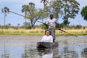 kanu mit frau und einheimischen steuermann der eine lange stange zum steuern in den händen hält auf dem wasser in botswana