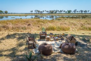 picknick decke mit kleinen stühlen und kissen inmitten der natur afrikas mit leckereien am hinteren ende der decke lädt zum essen verweilen und genießen der natur ein