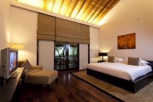 großes schlafzimmer mit terrassentüren sitzecke und tv in warmen farben und viel licht bei nacht