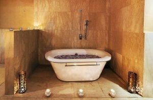 freistehende badewanne im spa bereich wellness mit wasser gefüllt und blüten darn im hellem raum mit steinwänden und kerzenlicht