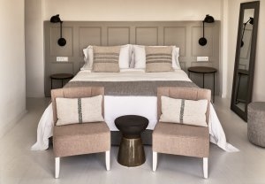 schlafzimmer in warmen erdtönen und moderner einrichtung vor dem großen bett zwei stühle in der aegean suite des luxushotels vedema