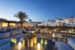 gemütliche terrasse des alti restaurant im luxushotel vedema bei nacht mit vielen kerzen und lichtern im hintergrund palmen und weißen häusern auf santorini