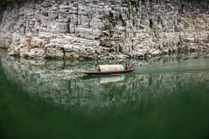 kleines fischerboot vor einer felswand im grünen wasser des flusses darauf ein fischer am steuer