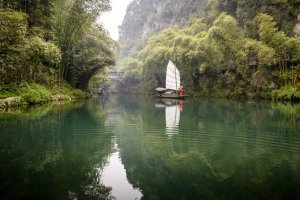 blick auf ein typisch chinesisches segelboot auf dem wasser umgeben von saftig grüner natur