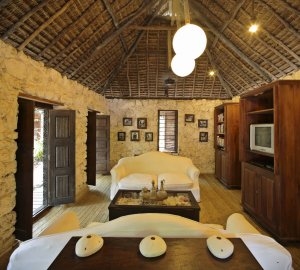 Wohnbereich in der andBeyond Mnemba Island Lodge auf Sansibar mit hellen Steinwänden Holzdach Holzmöbeln und weißen Sofas