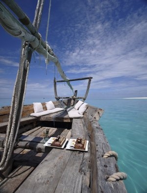Segelboot aus Holz auf dem türkisfarbenen Meer bei Mnemba Island das mit weißen Sitzecken zum träumen und entspannen unter blauem Himmel einlädt