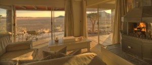 gemütliches und helles Zimmer 6 mit Wohnbereich Kamin und Terrasse großen Fenstern sowie Blick in die Wüste Namibias für ihren Namibia luxus urlaub