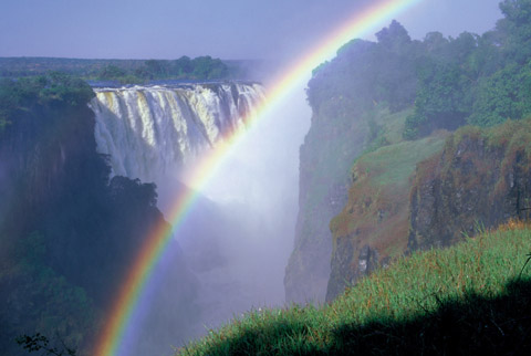 rauschender wasserfall der victoria falls mit regenbogen bei sonnenschein auf der afrika rundreise