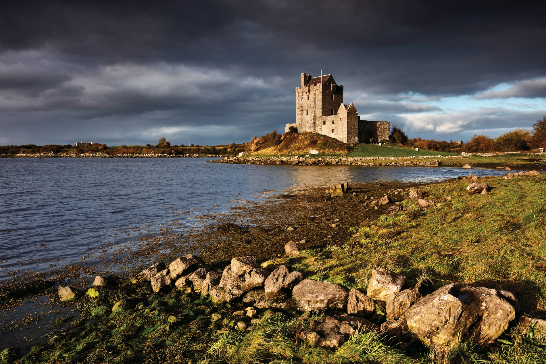 blick auf eine mittelalterliche burg in irland direkt am wasser mit dunkel bewölktem himmel