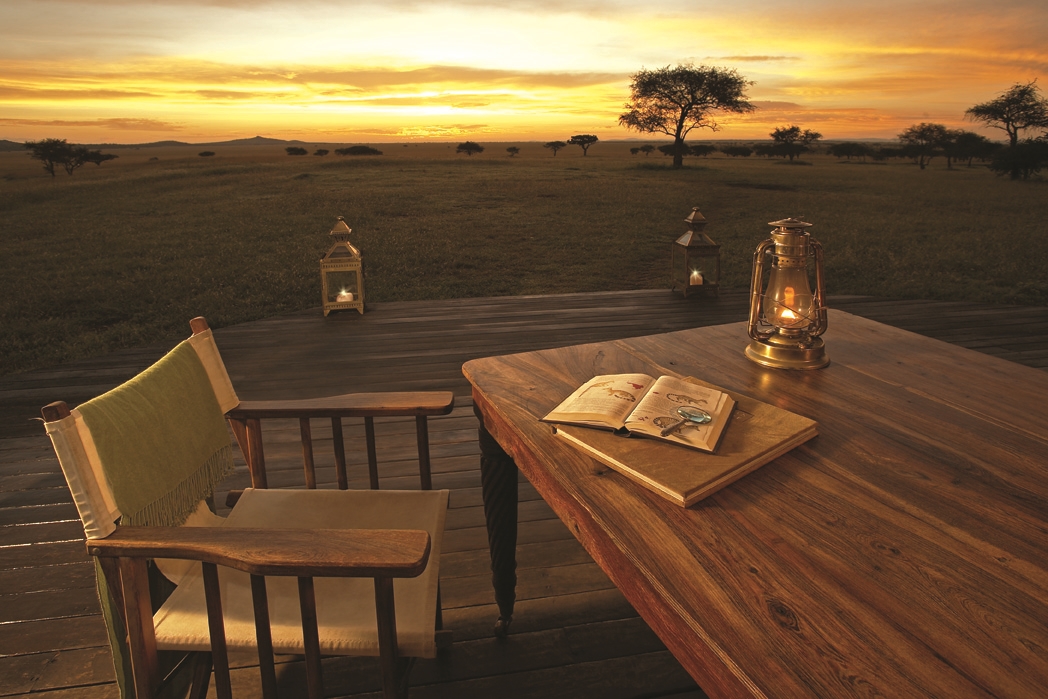 holzterrasse mit tisch und stuhl bei sonnenuntergang und öllampe bieten einen weiten blick in die abendliche naturschönheit von afrika
