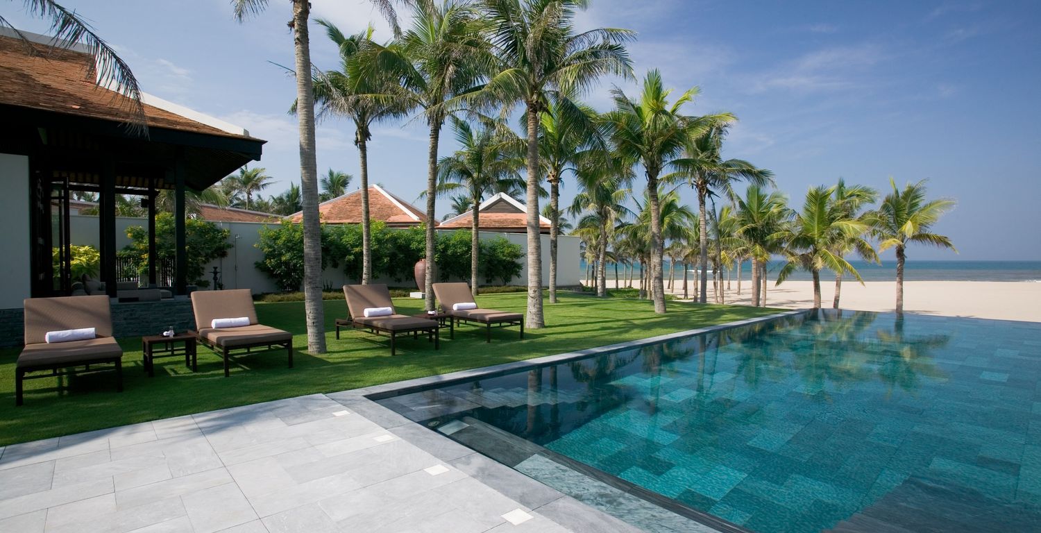 edler und moderner pool am strand von vietnam mit palmen umgebener pool in dunkelblau bis grünen farbtönen mit blick auf das meer